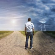image of man standing a a fork in the road. one is a sunny path and the other is a stormy path.