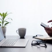 photo of someone texting on cell phone with a laptop in the background