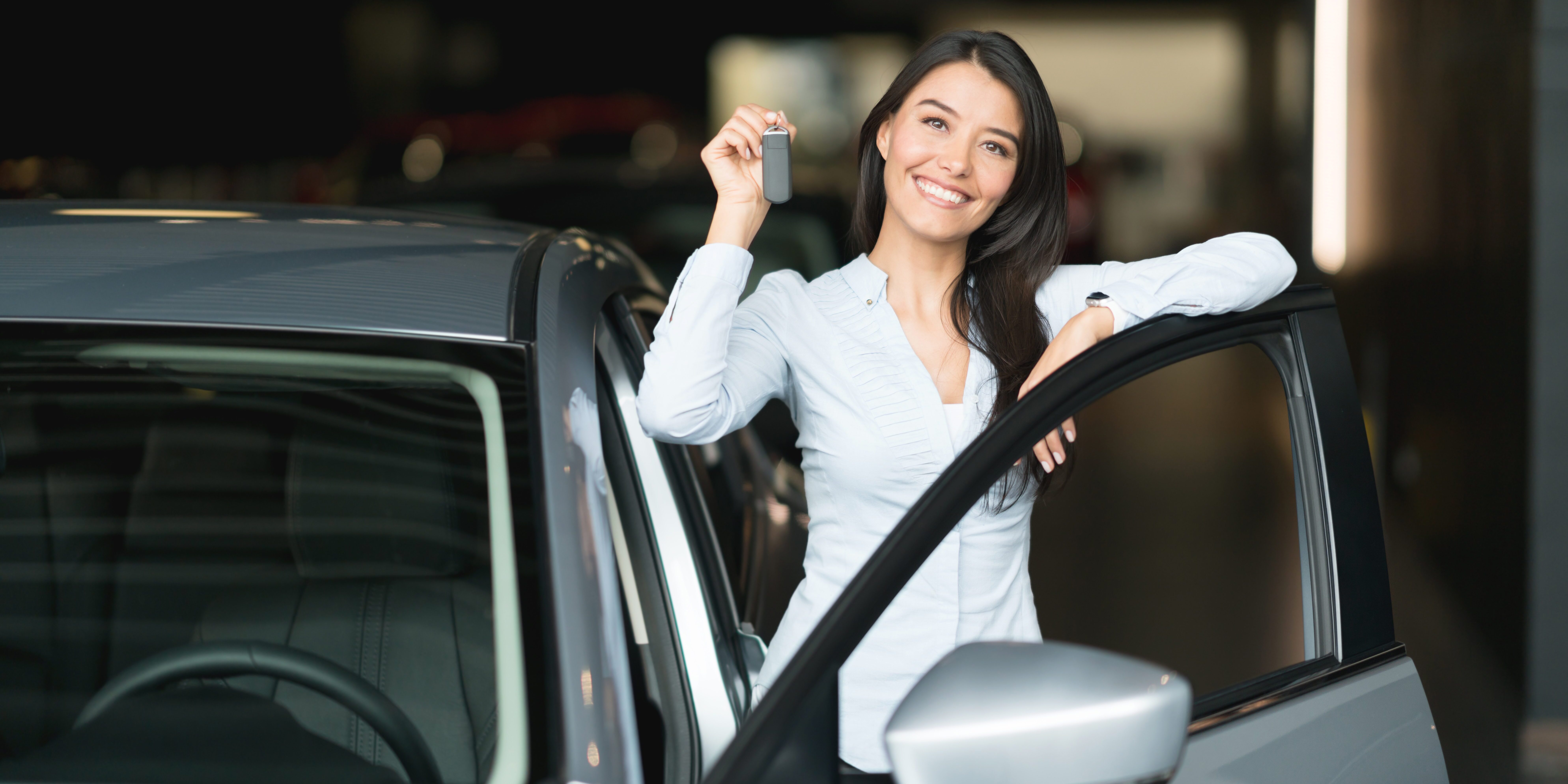 Portrait of a happy woman holding keys to her new car at the dealership