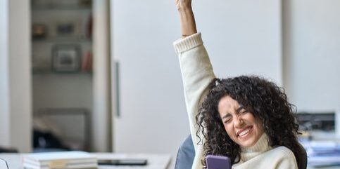 excited young lady holding a phone with her fist in the air