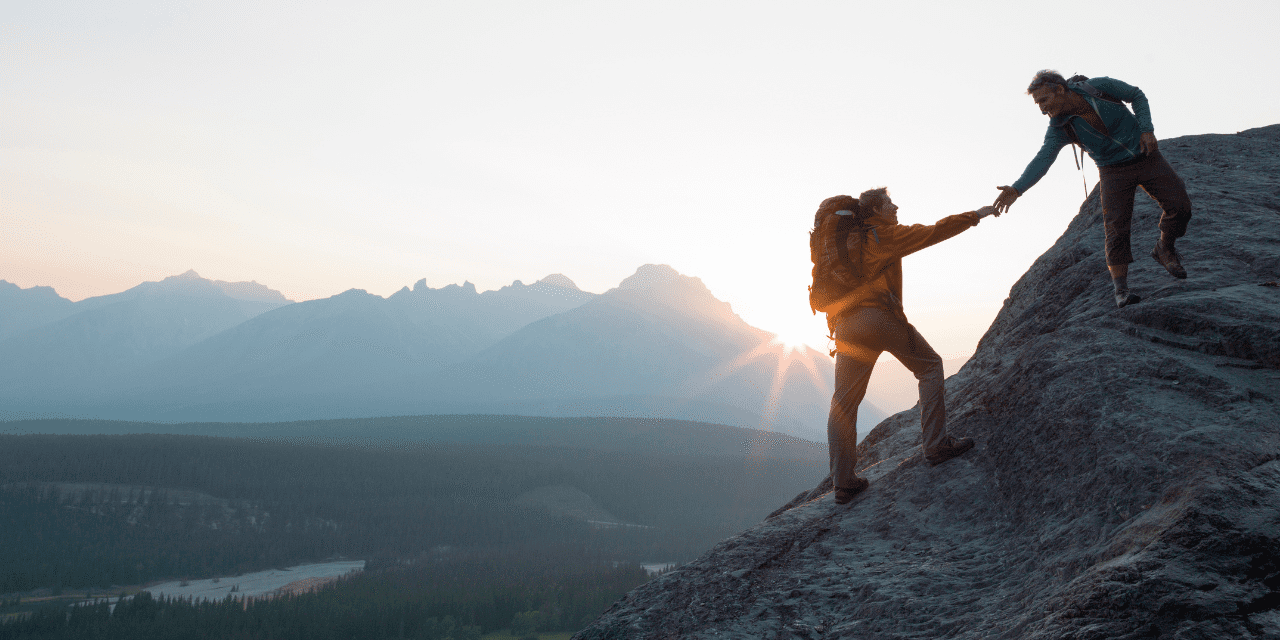 image of someone helping another person climb a mounting