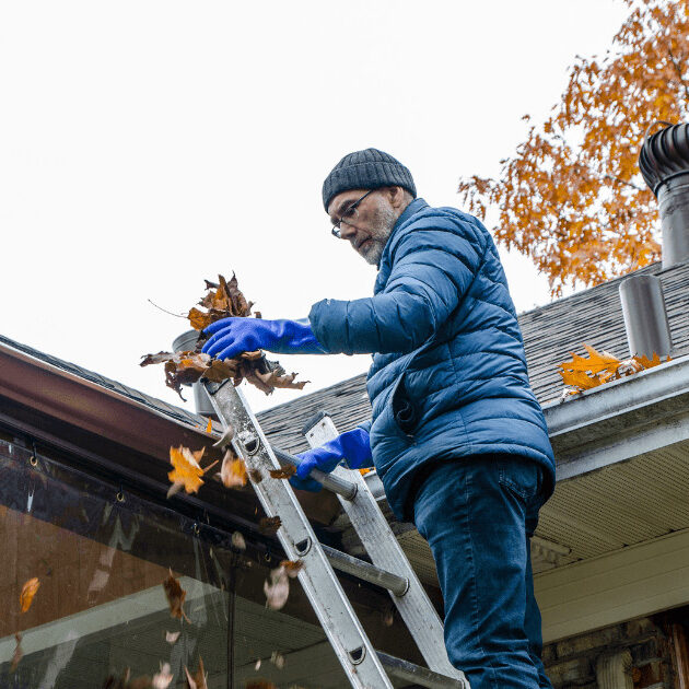 man removing leaves from gutter in the midst of fall home renovations