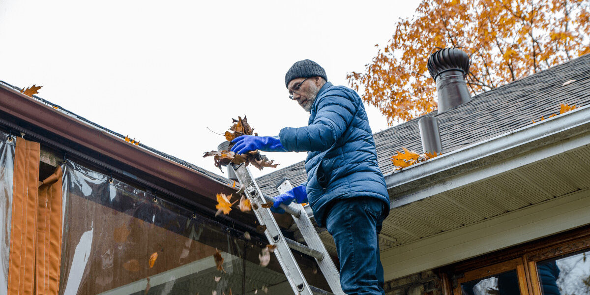 man removing leaves from gutter in the midst of fall home renovations
